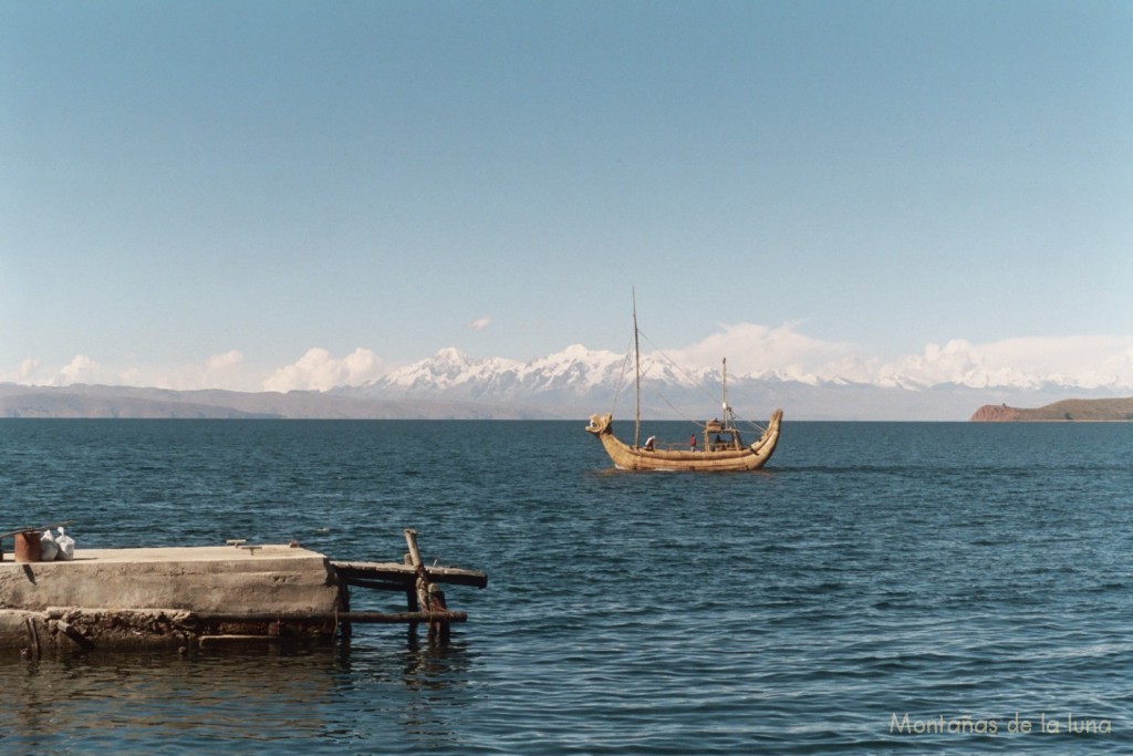 Llegando al puerto de la Isla del Sol, una totora navegando en el Lago Titicaca y al fondo izquierda el Ancohuma e Illampú en los Andes